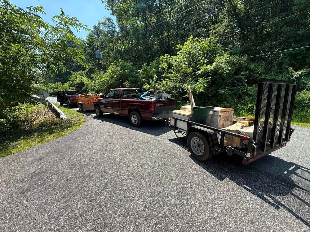 Two pickup trucks and a loaded dump trailer on a rural road during a property cleanup near Colora in Cecil County, Maryland