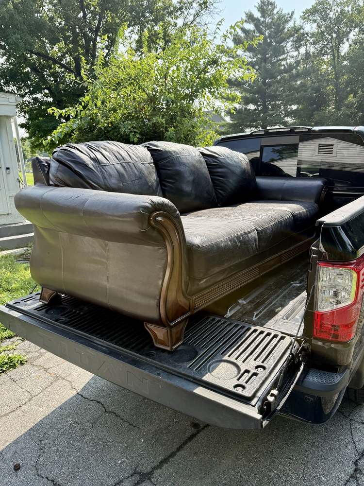 A worn black leather sofa loaded into the bed of a pickup truck on a driveway after a couch removal in Elkton, Maryland