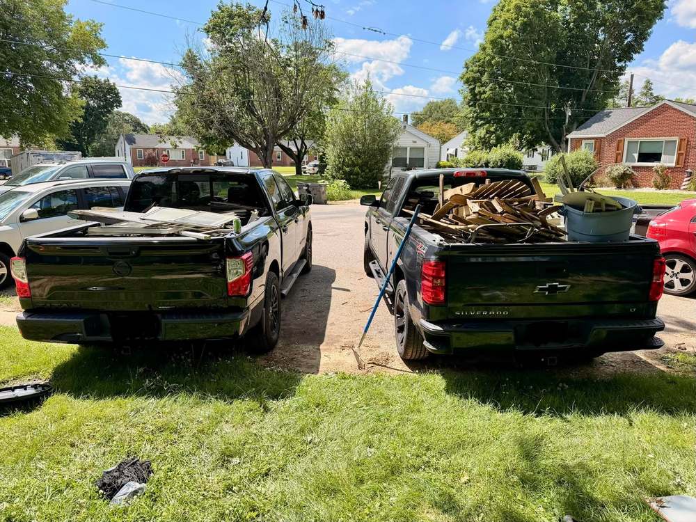 Two pickup trucks loaded with scrap lumber and old windows in a driveway after a property cleanup in Elkton, Maryland