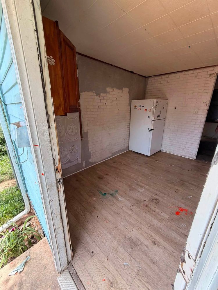 The side-door view of the Elkton kitchen after clearing, showing an empty floor and the refrigerator against bare brick