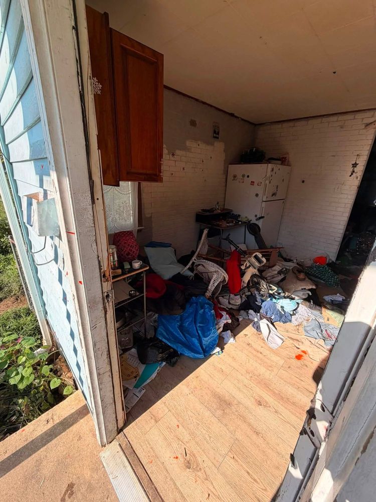 The same Elkton, Maryland kitchen seen from the side door, with furniture, bagged debris and clothing piled across the floor