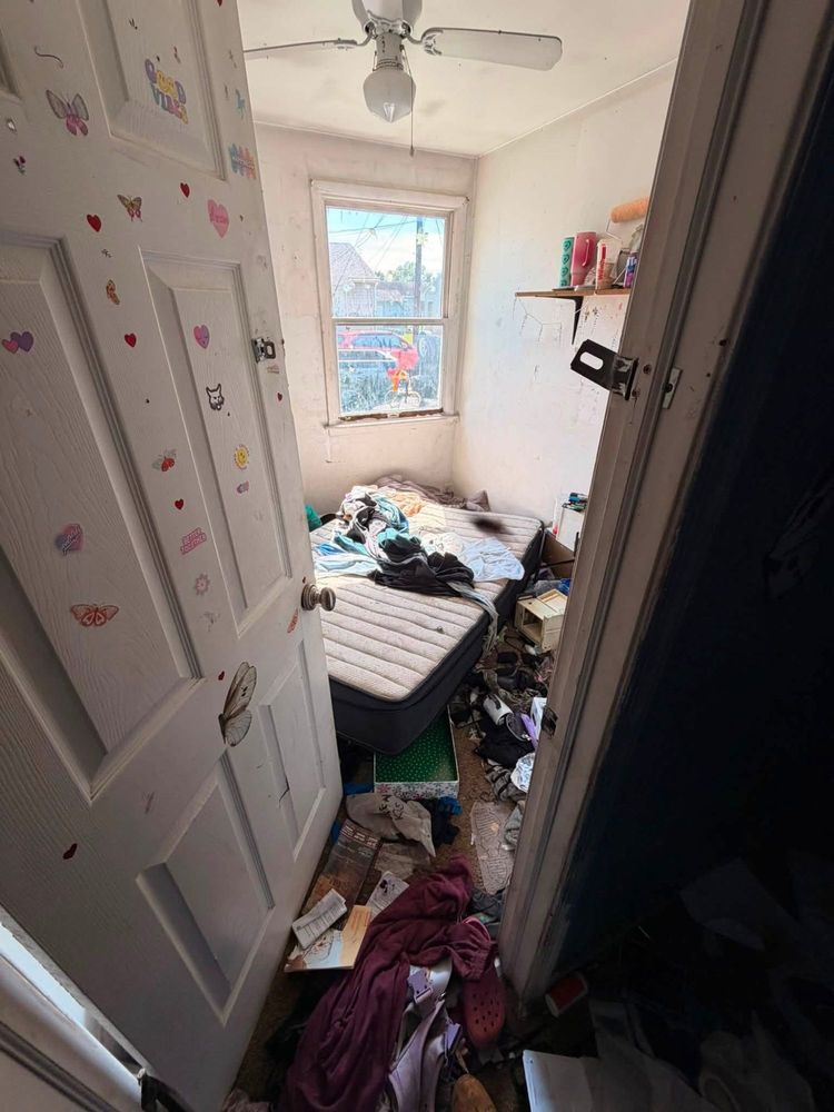 Small child&rsquo;s bedroom in an Elkton, Maryland hoarder house, with a sticker-covered door, a mattress on the floor and belongings across the carpet