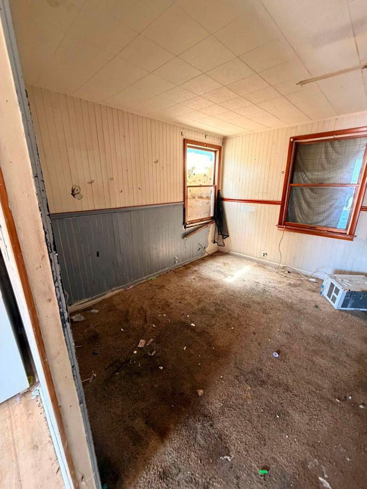 The same Elkton front bedroom cleared to bare carpet, with both windows uncovered and the gray wainscot wall visible