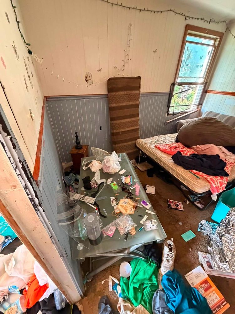 Front bedroom of an Elkton, Maryland hoarder house with a glass-topped table buried in small items, a mattress on the floor and butterfly decals on the wall