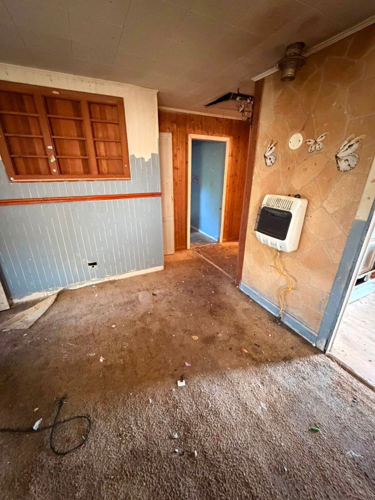 The same Elkton living room emptied to bare carpet, with the gas wall heater and display cabinet now clearly visible