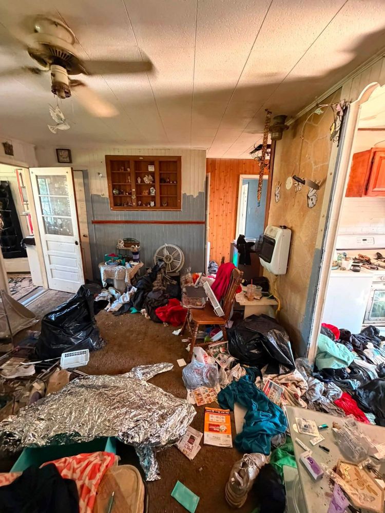Living room of an Elkton, Maryland hoarder house filled with black bags, clothing and furniture, with a gas wall heater and wooden display cabinet