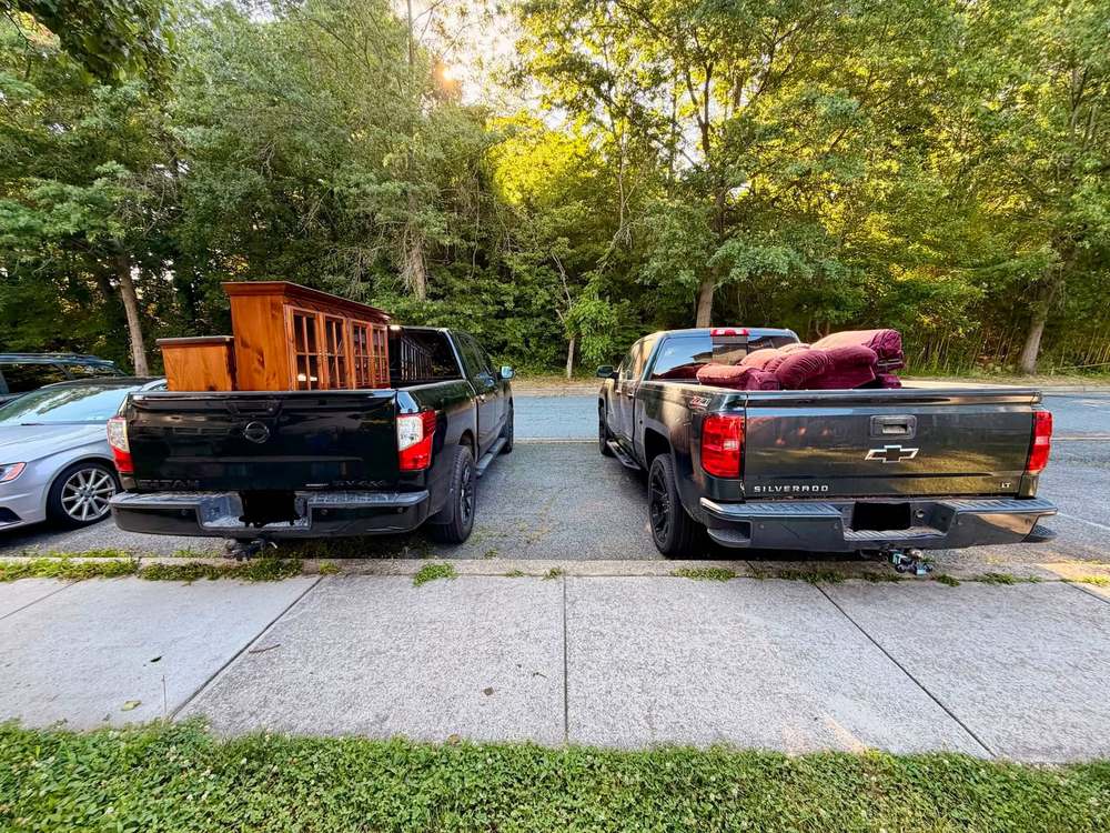 Two pickup trucks loaded with a wooden china cabinet and burgundy upholstered furniture after a furniture removal in North East, Maryland